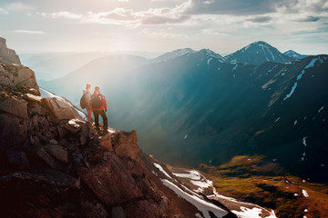 Two hikers stands on cliff in big mountains