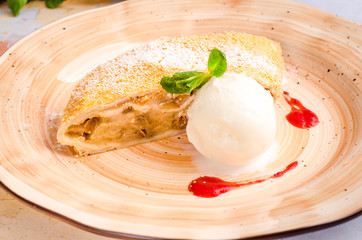 Delicious piece of apple strudel with vanilla ice cream, mint and berries on plate, close-up on a background teapot. Fresh baked homemade apple cake