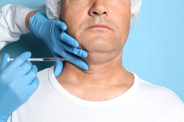 Mature man with double chin receiving injection on blue background, closeup