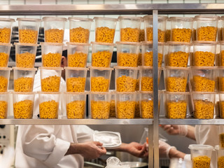 A lot of plastic containers with pasta on a stainless steel shelving in the kitchen in a...
