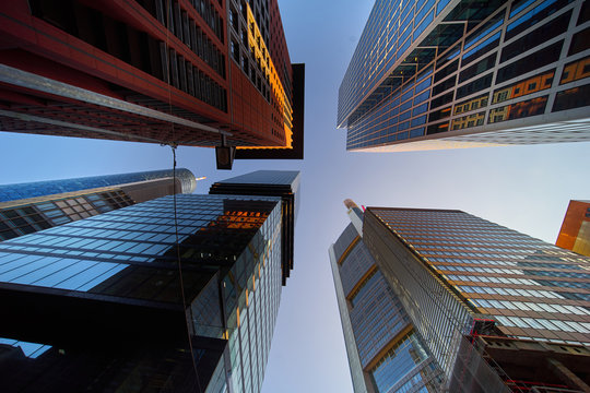 View of the small piece of free blue sky between four towers of high skyscrapers upwards