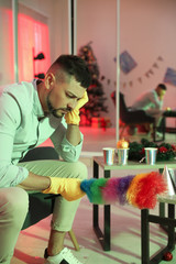 Man with dusting brush suffering from hangover in messy room after New Year party