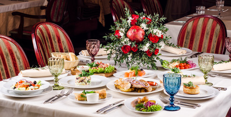 Served for holiday banquet restaurant table with dishes, snack, salads, cutlery, wine and water glasses. European food in a restaurant setting. Table set for an event party. catering