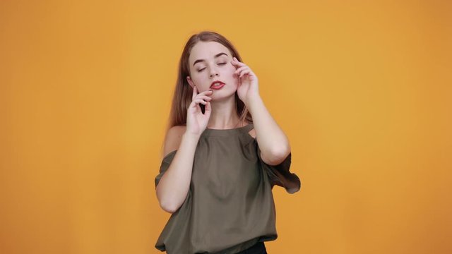 Young beautiful caucasian woman keeping hand on face, model gesture wearing haki shirt on isolated orange background