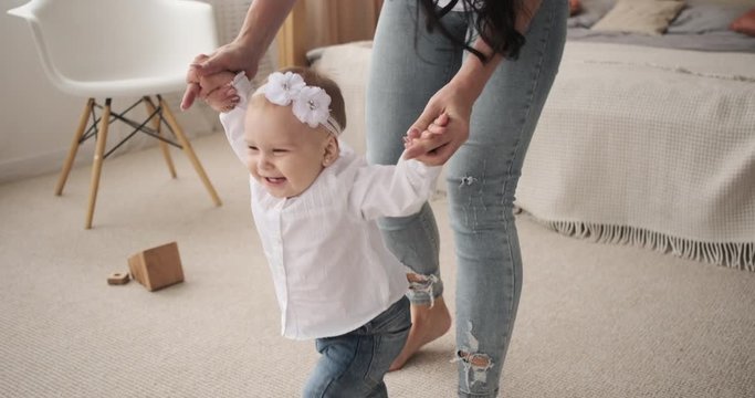 Mother holding hands of baby girl learning to walk for the first time at home