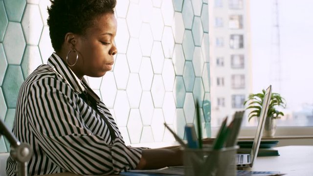 Concentrated african american woman typing on laptop while working at desk in the office