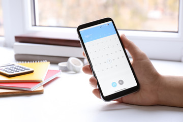 Woman using calendar app on smartphone indoors, closeup