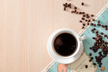 A white cup of coffee with coffee beans and map on wooden background