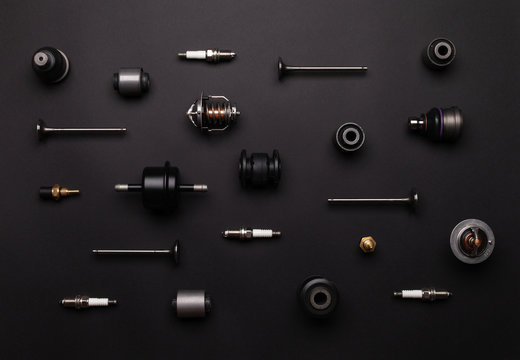 Studio photography - a lot of automotive parts: valves, spark plugs, silent blocks, thermostats, filter, sensors, ball bearings, lie in straight rows on a flat surface isolated on a black background.