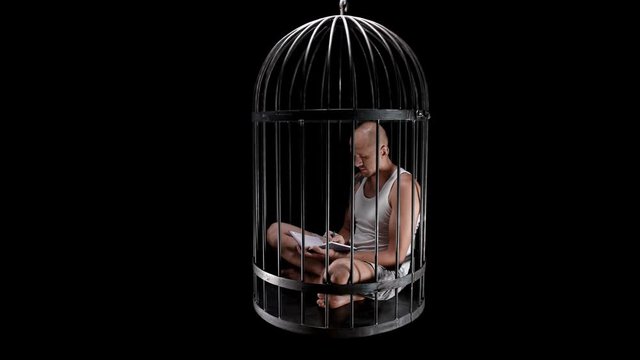 a person in a bird cage is in captivity, writes something in a notebook, maybe works, close-up, maybe each of us is locked in his own cage