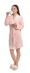 Young woman in bathrobe with cup of beverage on white background