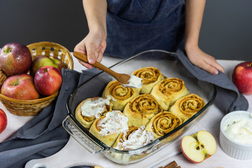 The process of glazing fresh baked cinnabon. Children's hands smear buns with cream. On a white wooden table nearby are yaloks, which are also in the filling.