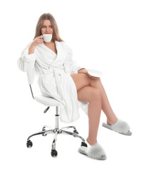 Young woman in bathrobe with cup of beverage on white background