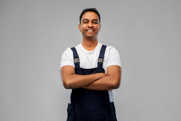 profession, construction and building - happy smiling indian worker or builder with crossed arms over grey background
