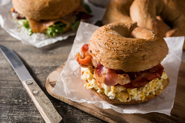 Bagel sandwich with bacon, egg and cheese on wooden table.	