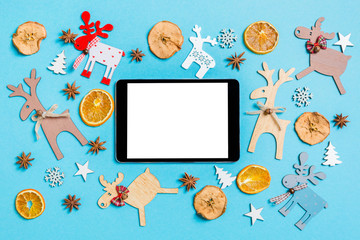 Top view of digital tablet on blue background made of holiday decorations and toys. Christmas ornament concept