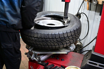 Concept Photography with a tire fitting. A worker is serving a car. He puts the tire on the wheel disc using a special machine and tool.