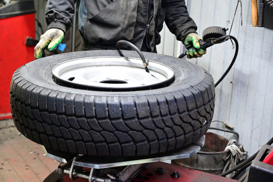 Concept Photography with a tire fitting. A worker is serving a car. He puts the tire on the wheel disc using a special machine and tool.