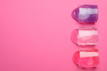 Overturned plastic containers with bright slimes on pink background, top view. Space for text