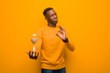 young african american black man against orange wall with a sand clock timer
