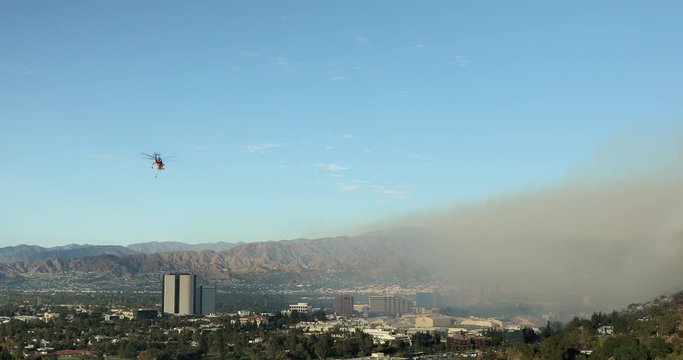 November 9, 2019. A firefighter helicopter approaches a burning area through a smoky sky and dumps tons of water onto a blazing forest. Hollywood hills. Warner Brothers wildfire. Los Angeles County.4K