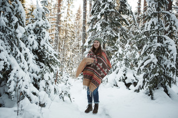 Beautiful woman among snowy trees in winter forest and enjoying  snow. Wearing plaid scarf and parka. Hipster boho style