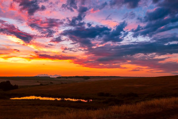 Bright colorful dramatic landscape. The sky at sunset in the evening, blue, purple, orange with thunderclouds before the storm, fields and meadows, the sun sets over the horizon