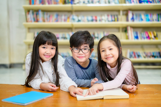 Asian Kids Reading Book in School Library with a Shelf of Book in Background, Asian Kid Education Concept