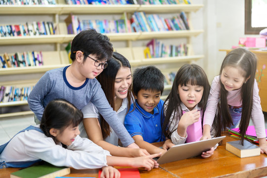 Group of Asian Student Kid Learning to use Laptop in Library with Women Teacher, Shelf of Books in Background, Asian Student Education Concept
