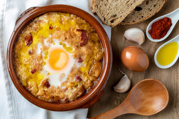 Garlic and bread soup (Castilian, from Spain) in clay pot and its main ingredients. View from above. Wood background