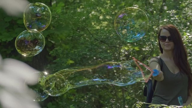 Pretty woman making Colorful Big shimmering Soap Bubbles in the forest. Background Green Trees. Slow Motion. Prores 10Bit mov.