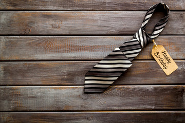 Happy birthday text near male tie on dark wooden background top view copy space