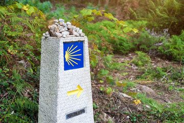 Yellow scallop shell, touristic symbol of the Camino de Santiago showing direction on Camino Norte in Spain.Column with rocks signing the way to Santiago De Compostela on the St James pilgrimage route - obrazy, fototapety, plakaty