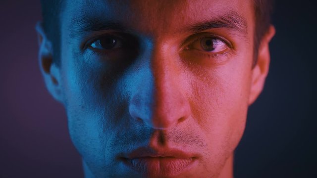 Close-up portrait of handsome young man looking at camera with serious and confident expression on his face in trendy neon pink and blue lights.