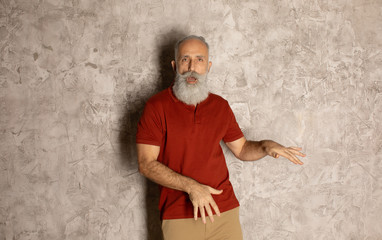 Happy cheerful bearded elderly man dancing on grey wall.