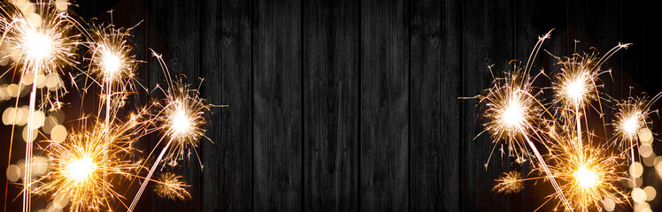 Silvester background banner panorama long- sparklers and bokeh lights on rustic wooden texture, top view with space for text
