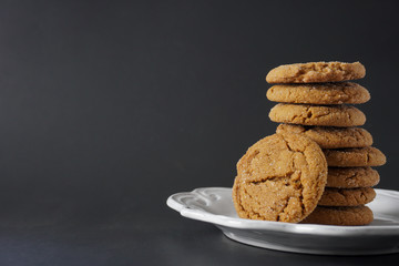 A gingerbread cookie leans against a stack of cookies on a white plate with a black background with copy space