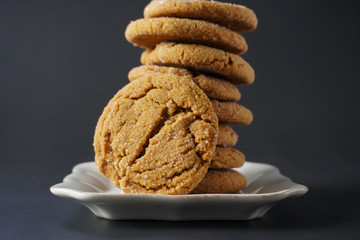 Close-up of the face of a gingerbread cookie leaning against a stack of cookies on a white plate with a black background