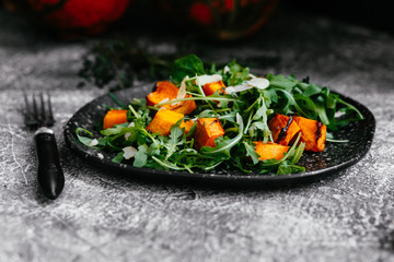 Baked pumpkin vegetarian salad with arugula and nuts in a plate on the table