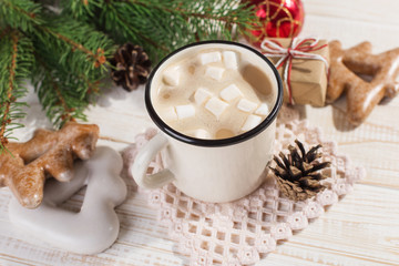 Hot Christmas drink with marshmallows in an iron mug and gingerbread cookies, on a white table. New Year, holiday background, copy space.
