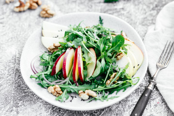 Vegetarian salad of fresh apples with arugula, onions and nuts in a plate on the table