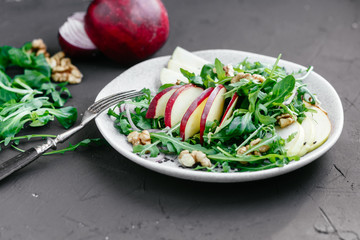 Vegetarian salad of fresh apples with arugula, onions and nuts in a plate on the table