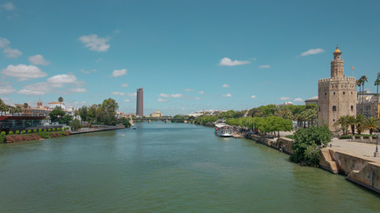 Obraz premium Views of the city from the bridge Puente San Telmo over Guadalquivir river towards watchtower Torre del Oro, Triana bridge and neighborhood and Cajasol Tower, in Seville, Andalusia, Spain
