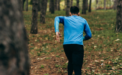 Rear view image of runner man running outdoor in the forest background. Fitness male exercising in the park, wearing blue and black sportswear. People and sport concept