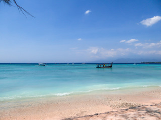 A boat parked next to the shore on Gili Air, Lombok, Indonesia. Beautiful and clear water. In the back visible Mount Rinjani. Some trees on the shore, few clouds on the sky. Holidays paradise.
