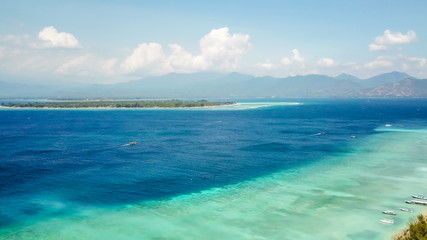 A drone shot of white sand beach on Gili Air, Lombok, Indonesia. Beautiful and clear sea water. There is a boat anchored to the beach. In the back visible Mount Rinjani. Holidays paradise.