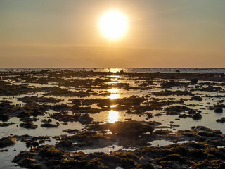 Obraz premium Sunset on Sengigi beach on the island of Lombok in Indonesia. Beautiful warm colored sunlight reflections on the water surface. The sea water is very shallow, some small reefs coming out of it.