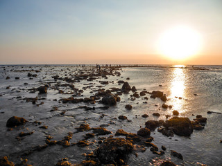 Fototapeta na wymiar Sunset on Sengigi beach on the island of Lombok in Indonesia. Beautiful warm colored sunlight reflections on the water surface. The sea water is very shallow, some small reefs coming out of it.