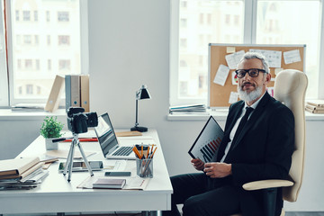 Confident mature man in elegant full suit looking at camera while making social media video