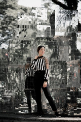 Fototapeta na wymiar street portrait, strong woman in black, confident woman, lady in city, portrait of Asian female, posing in front of glass mirror wearing black white stripe top and black pants, sporty girl